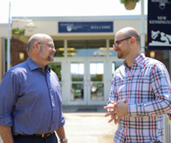 Two men speak in front of a building